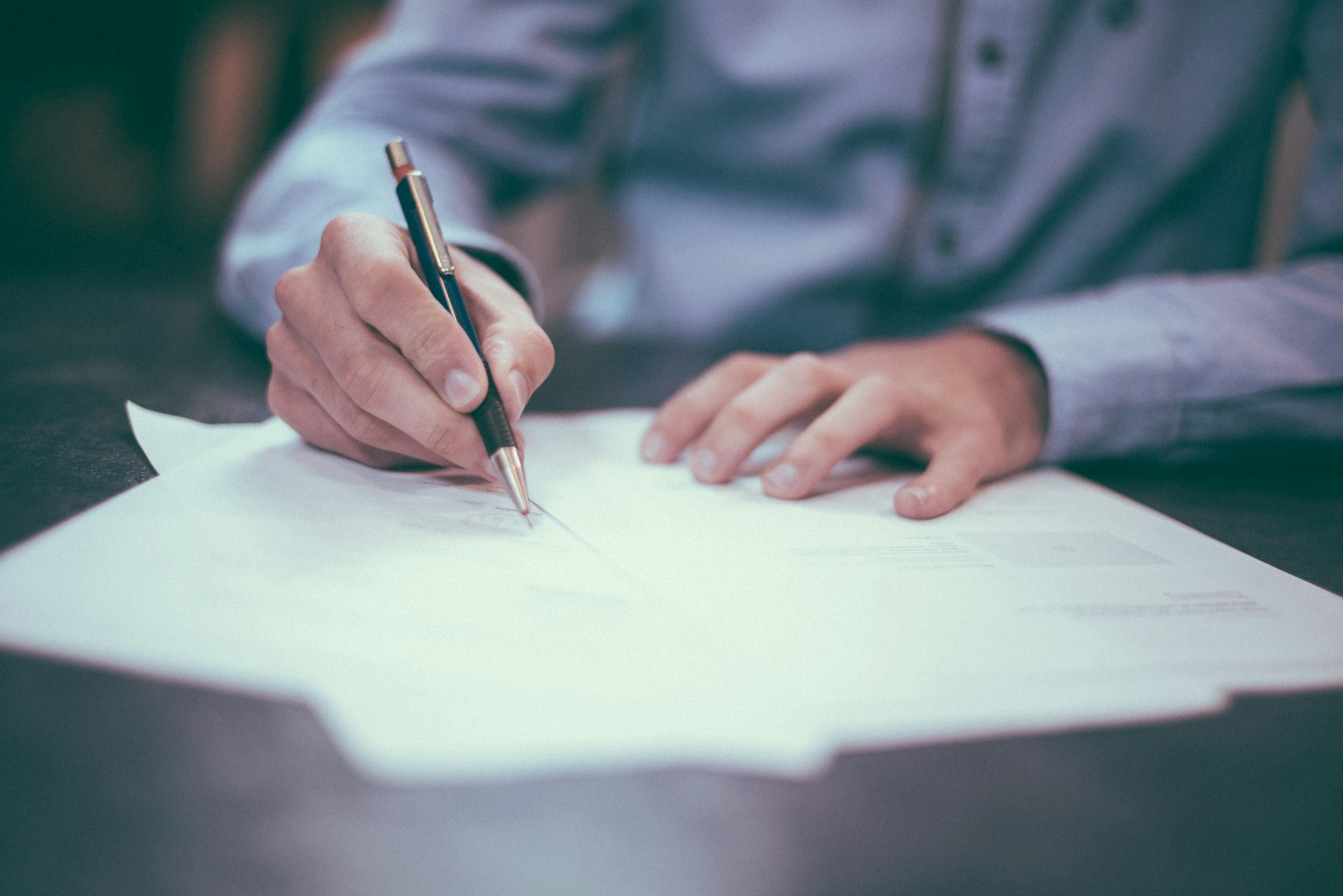 Main signant un document au stylo sur un bureau sombre, faible profondeur de champ