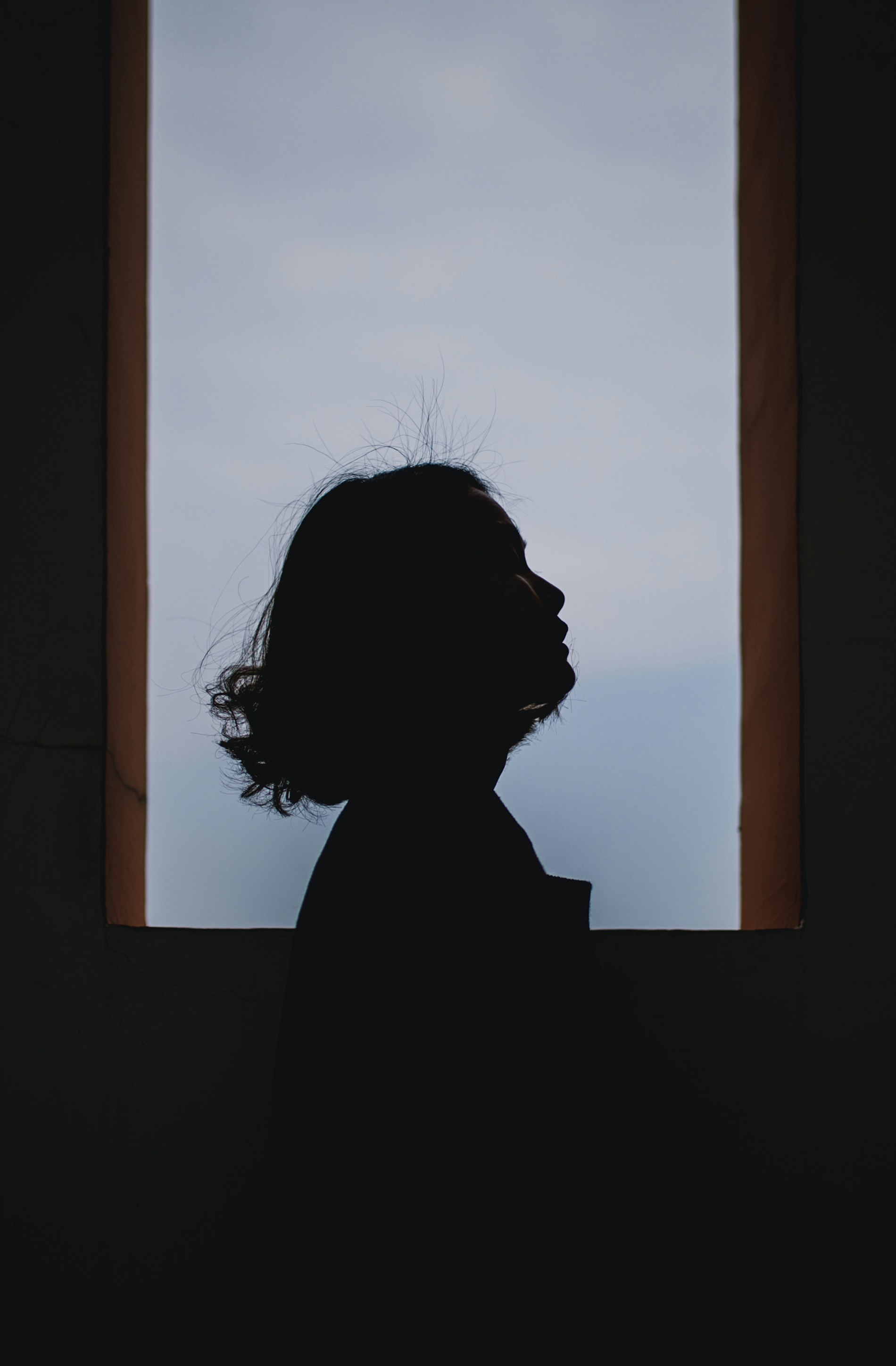 Silhouette de profil, visage levé, respiration calme devant une lumière bleu-gris